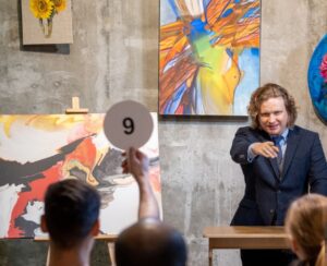 Image of an art auction with people raising their paddles for the blog Top 6 Essentials When Buying Art